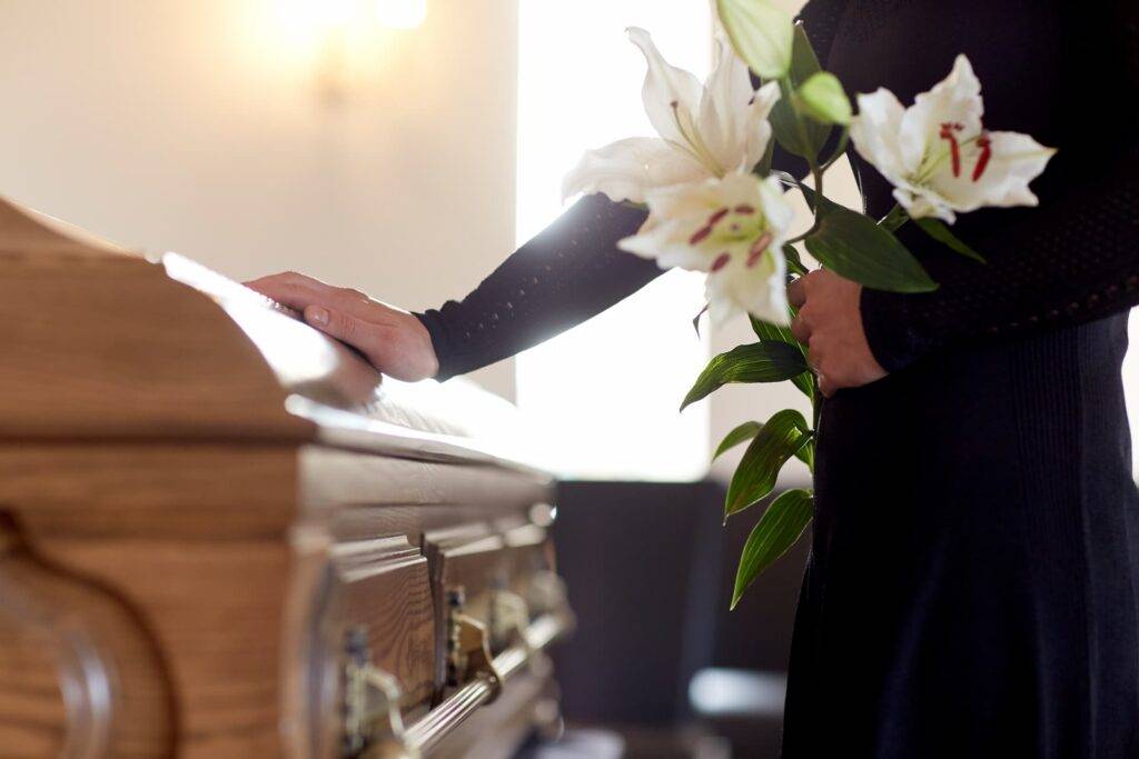 person holding flowers with hand on coffin